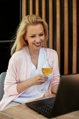 Takım elbiseli, şarap içen ve dizüstü bilgisayarla çalışan güzel bir iş kadını. İş kadını restoranda eğleniyor.
