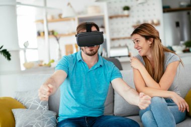 Mutlu çift oturma odasında sanal gerçeklik gözlükleriyle eğleniyor. Evde video oyunu oynayan ve eğlenen genç bir çift..