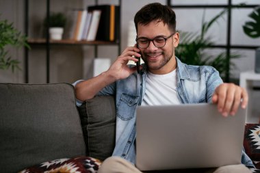 Oturma odasında dizüstü bilgisayarlı gözlüklü genç adam.