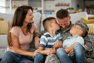 Mutlu asker ailesiyle birlikte yerde oturuyor. Asker ve karısı evde çocuklarla eğleniyor.
