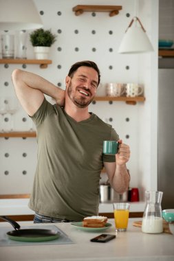 Yakışıklı adam mutfakta kahve içiyor ve esniyor. Genç adam sabah eğleniyor..