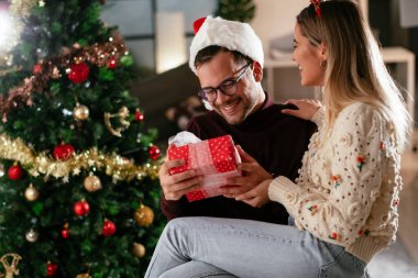 Genç adam ve kız arkadaşı Noel süslemeli oturma odasında hediye kutusuyla
