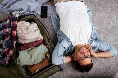 Yolculuğa hazırlanan adam, valizinin yanında yatıyor.