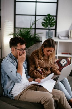 Genç adam ve kız arkadaşı kanepede kağıtlarla.