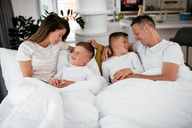 Genç bir aile yatakta eğleniyor. Oğulları yatakta dinlenen mutlu ebeveynler..