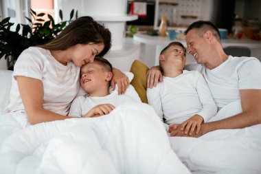 Genç bir aile yatakta eğleniyor. Oğulları yatakta dinlenen mutlu ebeveynler..