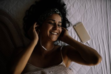 Yatakta müzik dinleyen bir kadın. Yatakta kulaklıkla uzanan güzel kız..
