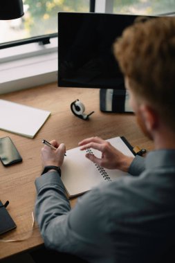 Genç kızıl iş adamı ofiste notlar alıyor.