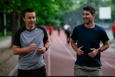 Gençler yarış pistinde antrenman yapıyor. İki genç arkadaş atletizm pistinde koşuyor.