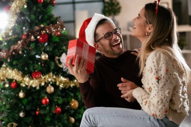 Genç adam ve kız arkadaşı Noel süslemeli oturma odasında hediye kutusuyla