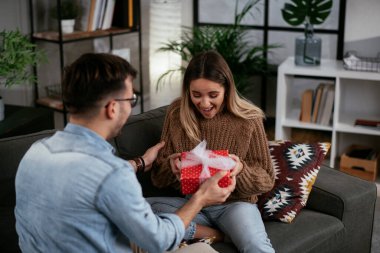 Genç adam ve kız arkadaşı oturma odasında hediye kutusuyla