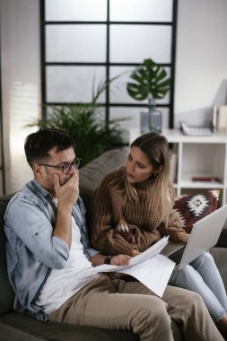 Genç adam ve kız arkadaşı kanepede kağıtlarla.