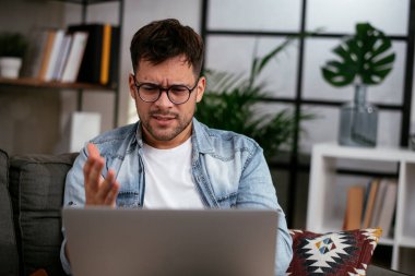 Oturma odasında dizüstü bilgisayarı olan stresli genç bir adam.