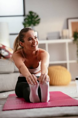 Spor kıyafetli atletik kadın evde spor egzersizleri yapıyor oturma odasında esneme egzersizleri yapıyor..