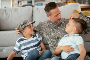 Üniformalı baba, oğullarıyla kanepede vakit geçiriyor. 