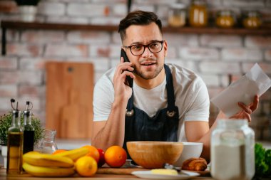 Yakışıklı adam mutfakta yemek pişiriyor ve cep telefonuyla konuşuyor..