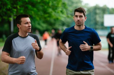 Gençler yarış pistinde antrenman yapıyor. İki genç arkadaş atletizm pistinde koşuyor.