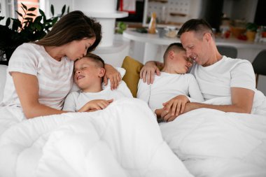 Genç bir aile yatakta eğleniyor. Oğulları yatakta dinlenen mutlu ebeveynler..