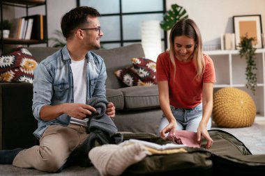 Genç adam ve kız arkadaşı oturma odasında bavul hazırlıyorlar.