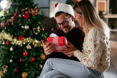 Genç adam ve kız arkadaşı Noel süslemeli oturma odasında hediye kutusuyla