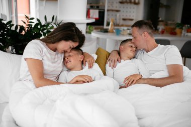 Genç bir aile yatakta eğleniyor. Oğulları yatakta dinlenen mutlu ebeveynler..