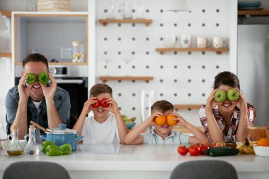 Anne ve baba oğullarla kahvaltı hazırlıyorlar. Genç bir aile mutfakta lezzetli yemekler hazırlıyor ve eğleniyor.