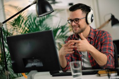 İş masasında kulaklık takan gözlüklü ve kareli gömlekli genç bir adam.