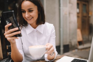 Kafede telefon kullanan güzel bir esmer. Gülümseyen genç iş kadınının portresi..