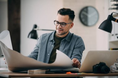 Çalışma masasında gözlüklü genç bir adam ve büyük bir kağıt çarşaf.