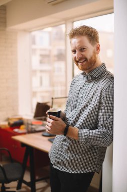 Kızıl saçlı yakışıklı işadamı ofiste kahve içiyor.