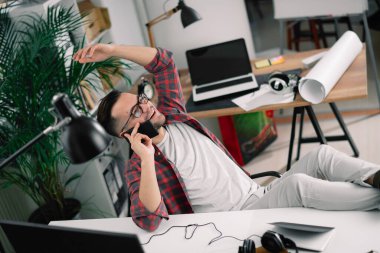 Genç adam çalışma masasında telefonla konuşuyor.