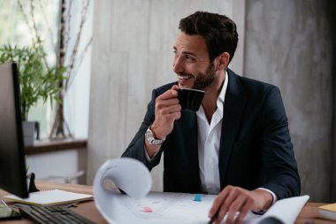 Genç iş adamı projeler üzerinde çalışıyor. Ofiste çalışan takım elbiseli yakışıklı bir iş adamı..