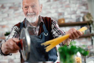 Yaşlı adam yemek yapıyor. Mutfakta kıdemli adam var..
