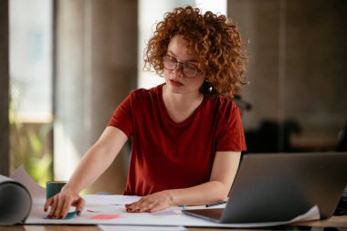 Güzel bir iş kadını proje üzerinde çalışıyor. Ofiste kıvırcık saçlı genç bir kadın var..