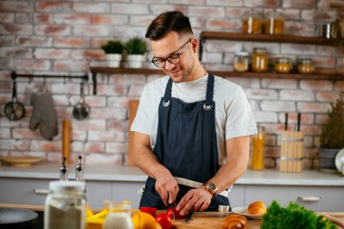 Mutfakta önlük giyen genç adam yemek pişiriyor.