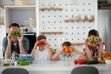 Anne ve baba oğullarla kahvaltı hazırlıyorlar. Genç bir aile mutfakta lezzetli yemekler hazırlıyor ve eğleniyor.