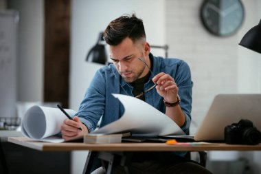 Çalışma masasında gözlüklü genç bir adam ve büyük bir kağıt çarşaf.