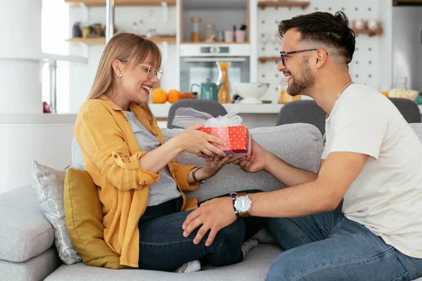 Man surprising his girlfriend with a gift. Young man giving gift box to his girlfriend.