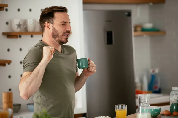 Handsome man drinking coffee in kitchen and yawn. Young man enjoying in morning.