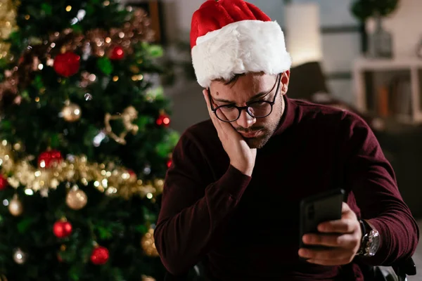 sad man in wheelchair by christmas tree with smartphone