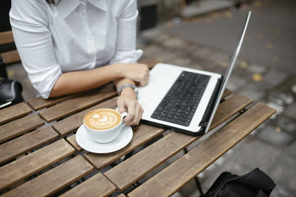 Woman sitting at cafe with laptop. Female hand on laptop and cup of coffee.