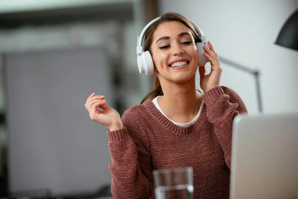 Young woman in office with headphones. Young casual businesswoman enjoying in her favorite song over headphones and singing while working on laptop in the office.