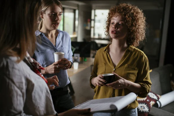 Girls talking and laughing in office. Beautiful women drinking coffee in the office