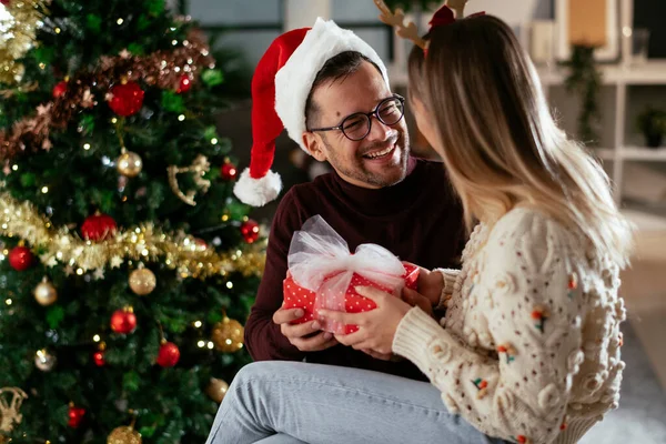 young man and his girlfriend with gift box in christmas decorated living room