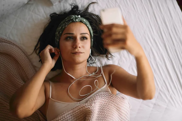Woman in bed listening music. Beautiful girl lying on bed with headphones.