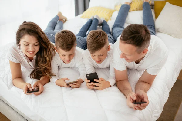 Family using mobile phones. Parents and kids using smart phones at home.