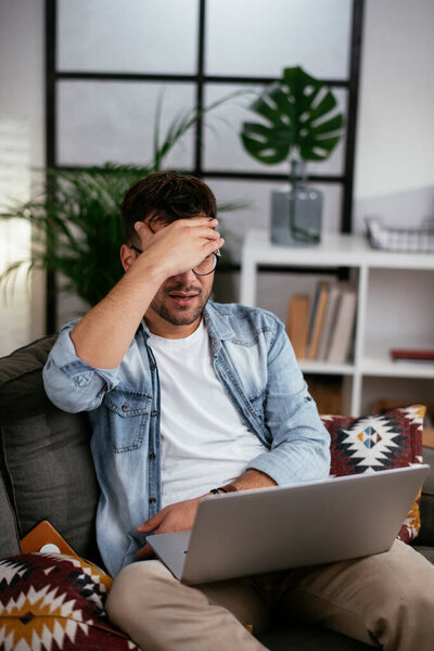 напряженный молодой человек с ноутбуком в гостиной