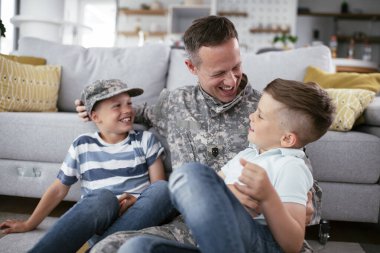 Mutlu asker ailesiyle birlikte yerde oturuyor. Evde çocuklarla eğlenen bir asker.