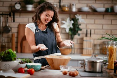 Gülümseyen kadın mutfakta yemek yapıyor.