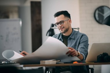 Çalışma masasında gözlüklü genç bir adam ve büyük bir kağıt çarşaf.